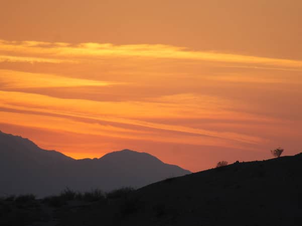 Desert sunset over mountains in Palm Springs, showcasing vibrant orange and yellow hues, highlighting the scenic beauty relevant to Covered Wagon Tours.